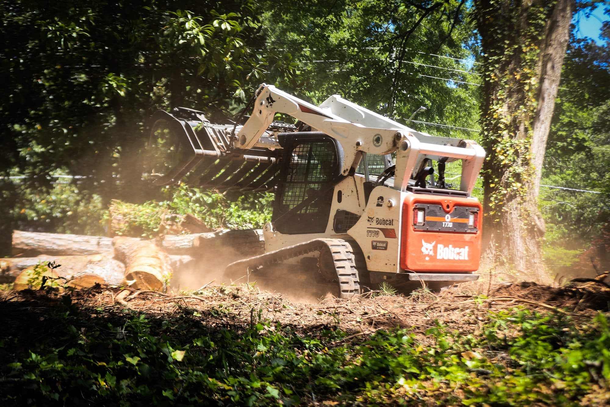 Skid steer with grapple attachment clearing felled logs and debris